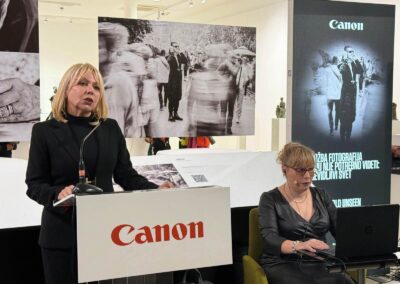 Фотографија са отварања светски значајне инклузивне изложбе „Невидљиви свет“ (World Unseen) компаније Canon у Галерији НКЈ. Приказани су посетиоци и званице у обиласку серије радова светских фотографа израђених у рељефној штампи. Кадар обухвата тактилне фотографије које слепи и слабовиди посетиоци доживљавају додиром, пропратне описе на Брајевом писму, као и посебне наочаре које посетиоцима симулирају различита оштећења вида ради подизања емпатије и свести о приступачности.