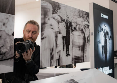 Фотографија са отварања светски значајне инклузивне изложбе „Невидљиви свет“ (World Unseen) компаније Canon у Галерији НКЈ. Приказани су посетиоци и званице у обиласку серије радова светских фотографа израђених у рељефној штампи. Кадар обухвата тактилне фотографије које слепи и слабовиди посетиоци доживљавају додиром, пропратне описе на Брајевом писму, као и посебне наочаре које посетиоцима симулирају различита оштећења вида ради подизања емпатије и свести о приступачности.
