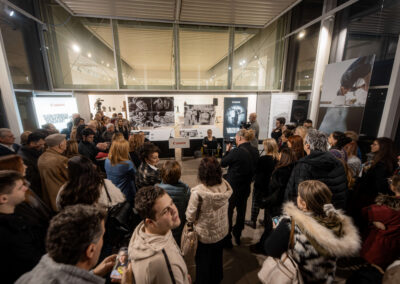 Фотографија са отварања светски значајне инклузивне изложбе „Невидљиви свет“ (World Unseen) компаније Canon у Галерији НКЈ. Приказани су посетиоци и званице у обиласку серије радова светских фотографа израђених у рељефној штампи. Кадар обухвата тактилне фотографије које слепи и слабовиди посетиоци доживљавају додиром, пропратне описе на Брајевом писму, као и посебне наочаре које посетиоцима симулирају различита оштећења вида ради подизања емпатије и свести о приступачности.